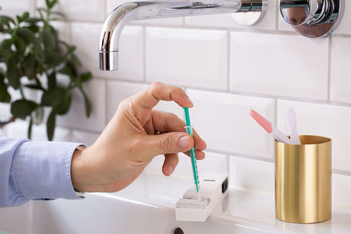 Bathroom setting with man applying sample to SwimCount device using semen syringe